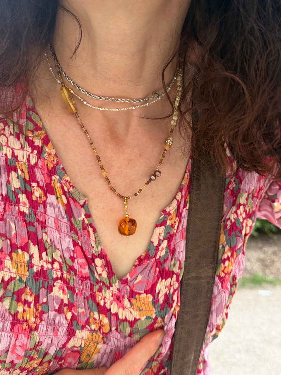 Nahaufnahme einer Kundin mit Bernstein Perlenkette und Bernsteinkugel-Anhänger von BARLA. Frau trägt rosa Blumenkleid