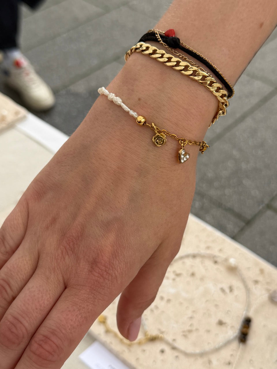 Nahaufnahme eines Handgelenks einer Kundin mit personalisiertem Armband aus Süßwasserperlen und zwei Charms: goldene Geburtsblume und Zirkonia Herz