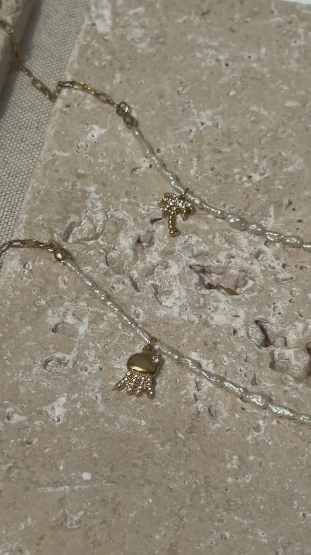 Zwei aehnliche Suesswassserperlen-Fusskettchen mit maritimen Charms liegen auf Naturstein